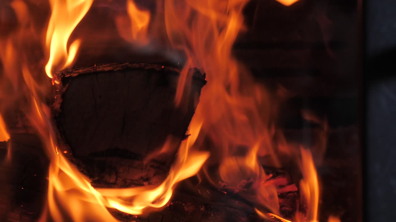 Up close shot of traditional household wood fire burning large piece of timber with red hot orange flames flickering in slow motion