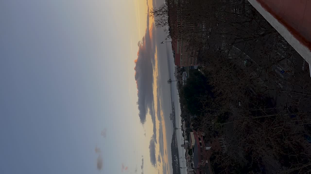 움직이는 구름, 나무로 둘러싸인 조용한 거리, 그리고 지평선에 있는 먼 건물과 함께 해가 지는 모습의 수직 타임스