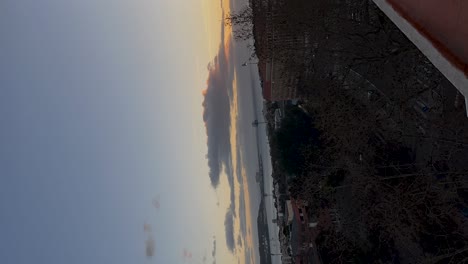 un lapso de tiempo vertical de una vista de puesta de sol con nubes en movimiento, una calle tranquila bordeada de árboles y edificios lejanos en el horizonte