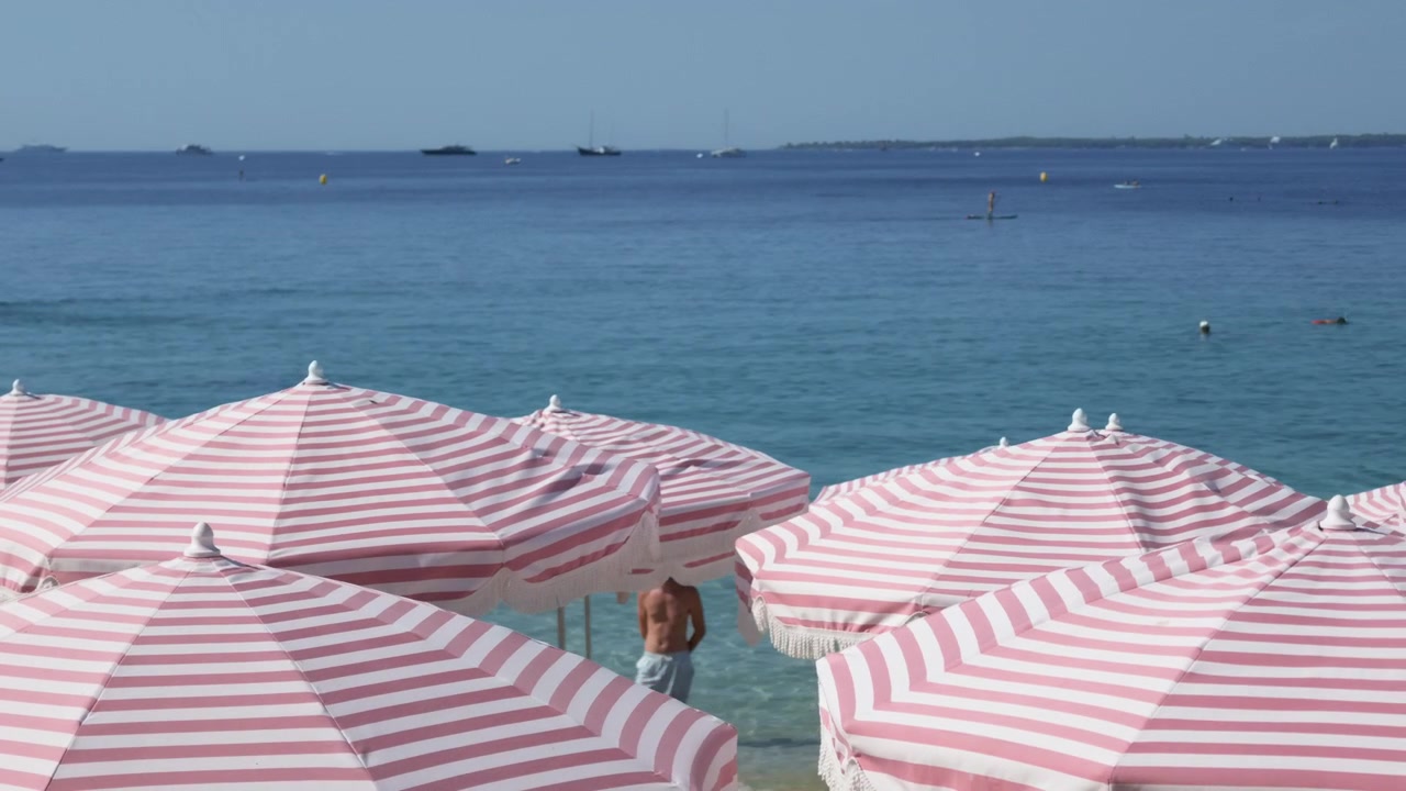 Primo piano di ombrelloni a strisce rosa e bianche con bagnanti e un paddleboarder in mare, Cannes, Francia