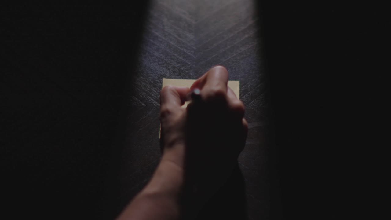 Slow motion close up footage of a hand writing out "Gobble Gobble" on a paper note and placing it on a table. Shot in dramatic lighting for an impressive title or transition