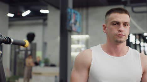 portrait view of well bodied man walking through gym hallway past people working out on weight machines and cardio equipment under bright led lights and industrial decor with small television on wall