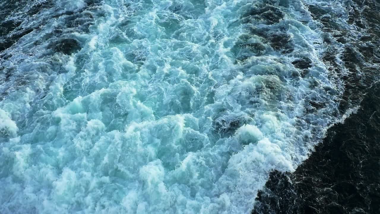 Tomada em tilt-up da grande esteira agitada da hélice na popa de um navio de cruzeiro até o horizonte, em câmera lenta.
