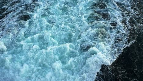 Tilt-up-shot-of-large,-churning-prop-wash-from-the-stern-of-a-cruise-ship-to-horizon-in-slow-motion