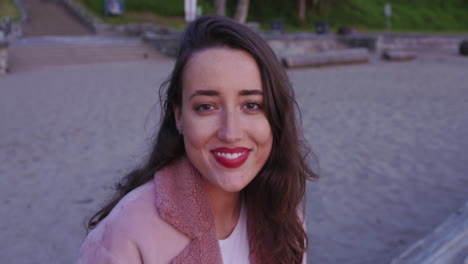 una hermosa mujer joven sentada en una playa gira y sonríe brillantemente a la cámara
