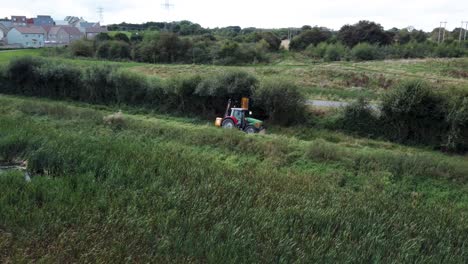 Tractor-in-field-trimming-hedges-on-overcast-day,-aerial-panning-shot