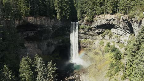 waterfalls over rocky ledge in dense forest during summer in british columbia, canada