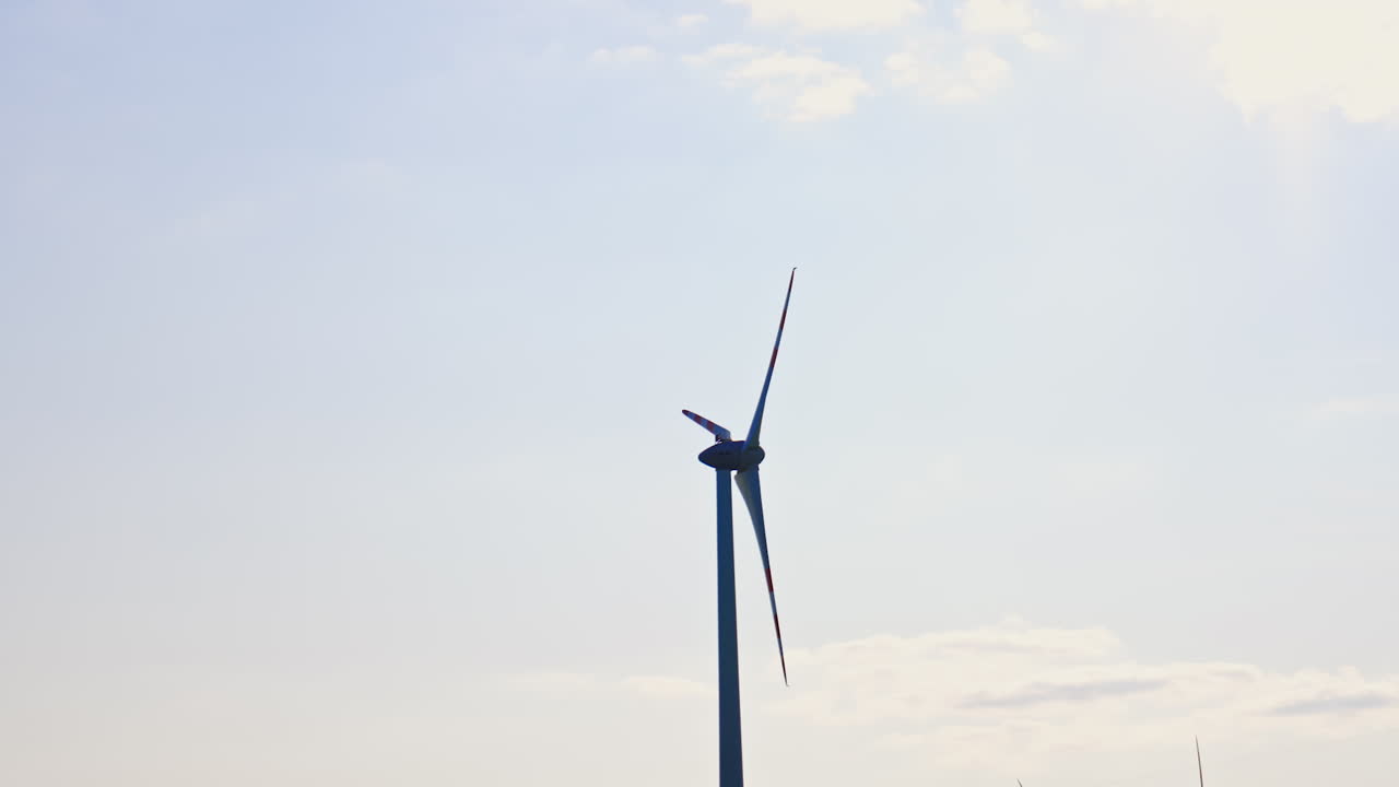 Wind turbine makes clean energy. A tall wind turbine stands against a clear sky, harnessing wind energy to produce electricity in a rural area