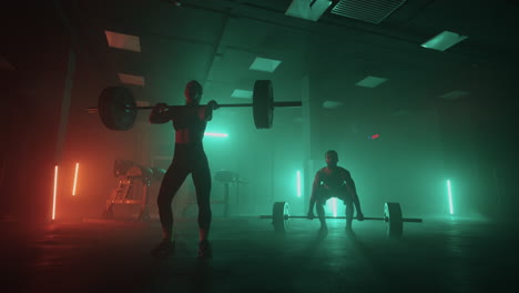a man and a woman together lift a barbell above their heads performing a jerk exercise from weightlifting. strong people in colored neon light train