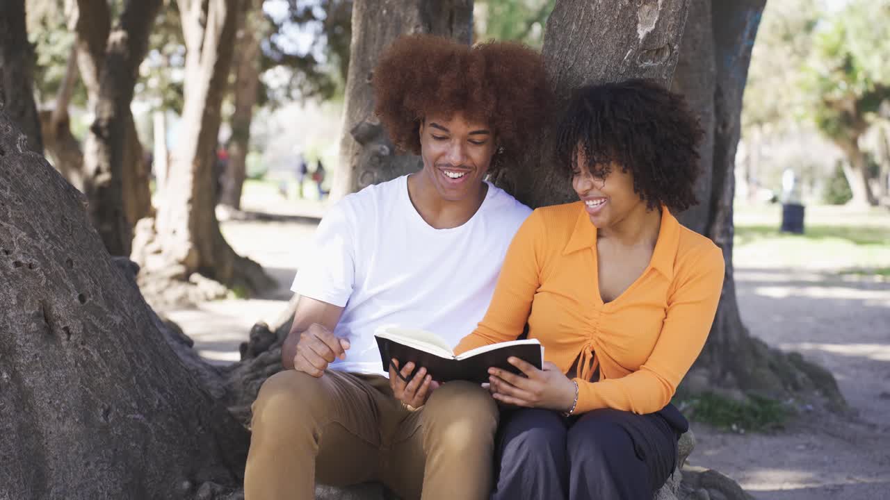 Happy black couple sitting looking at book on tree
