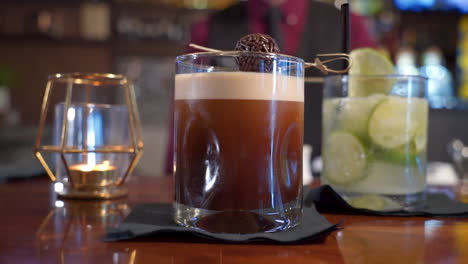 Two-beverages-on-bar-margarita-and-chocolate-coffee-cocktail-with-bartender-in-background,-slider-close-up-4K