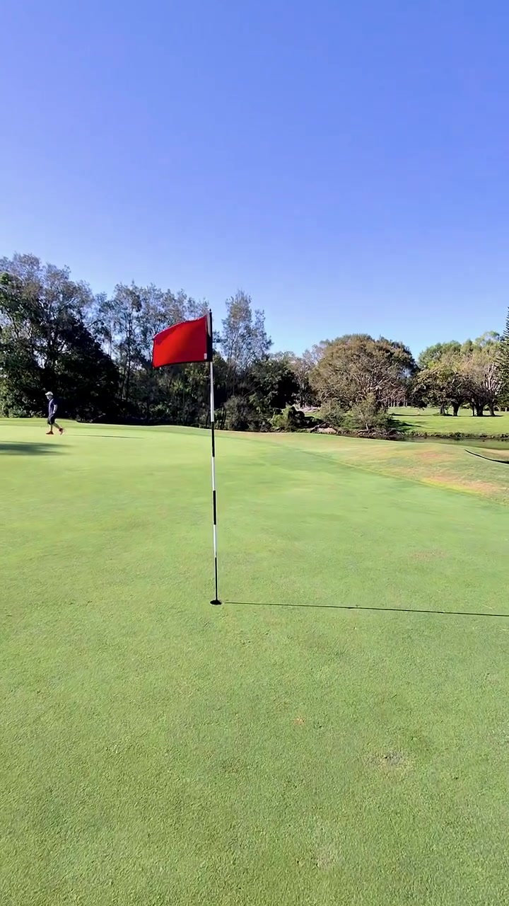 Campo lungo di un golfista che cammina su un luminoso green da golf verso l'asta della bandiera, con movimento della telecamera a mano.
