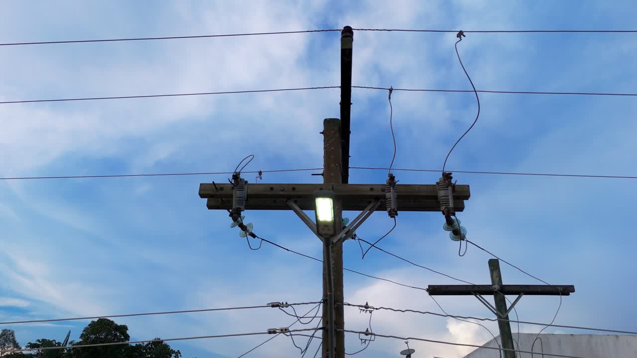 Aerial tilt view of rural power lines bringing electricity to homes and schools in a remote Amazonian settlement, highlighting essential infrastructure and jungle surroundings