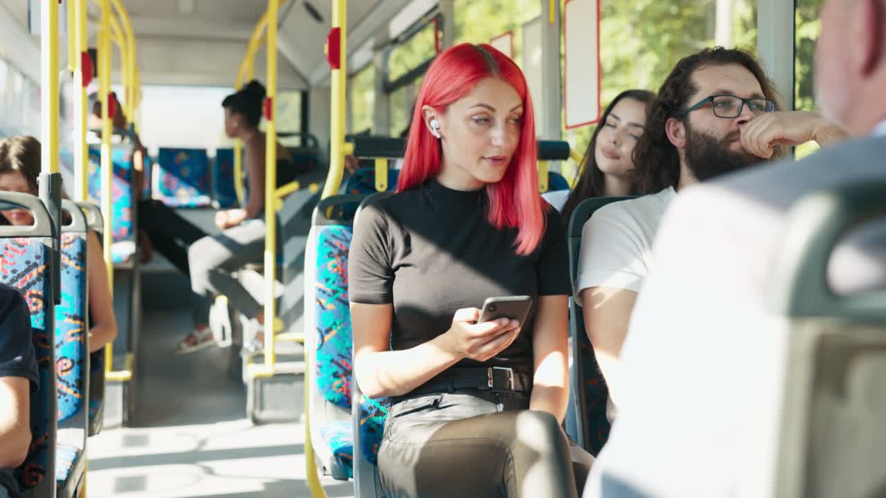 분홍색 머리카락을 가진 여성이 대중교통 버스를 타고, 소녀는 스마트폰을 사용하고, 무선 이어폰을 가지고 있습니다.