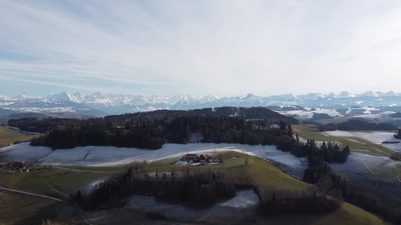 Slightly snow-covered, lush green meadows with the imposing Swiss Alps in the background, drone shot