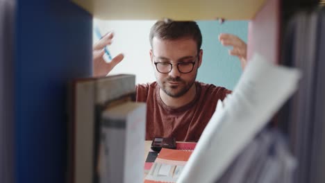a young man browses through documents and binders on a shelf, clearly searching for something important. his expression shifts to disappointment as he fails to find what he was looking for