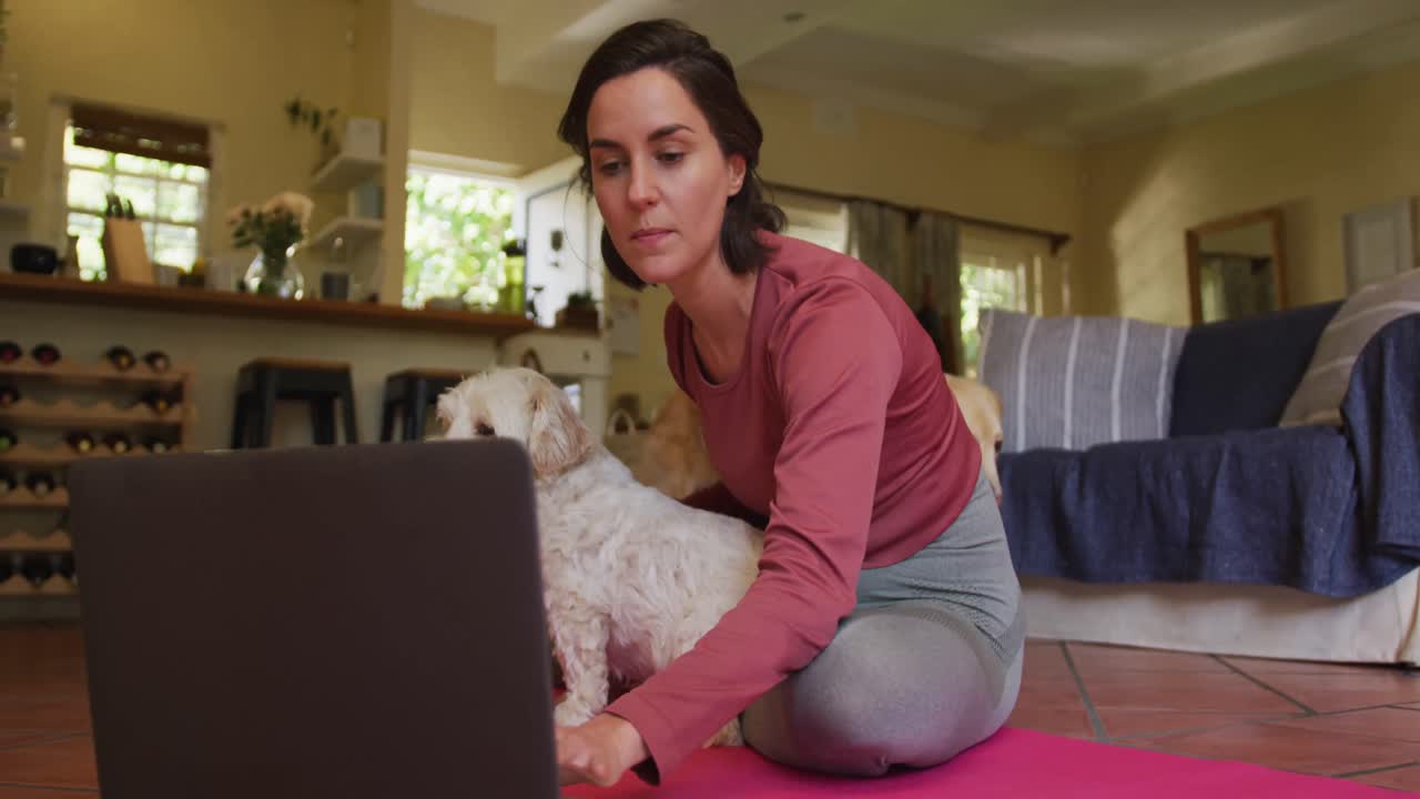 mujer caucásica haciendo ejercicio con su perro mascota usando una computadora portátil en casa