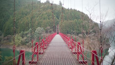 puente colgante rojo zaobashi que cruza el río arita con un exuberante bosque montañoso al fondo en wakayama, japón