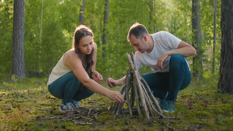 a couple man and a woman together collect a fire from sticks in the woods. a young couple in a hike puts a fire for the night and cooking in nature