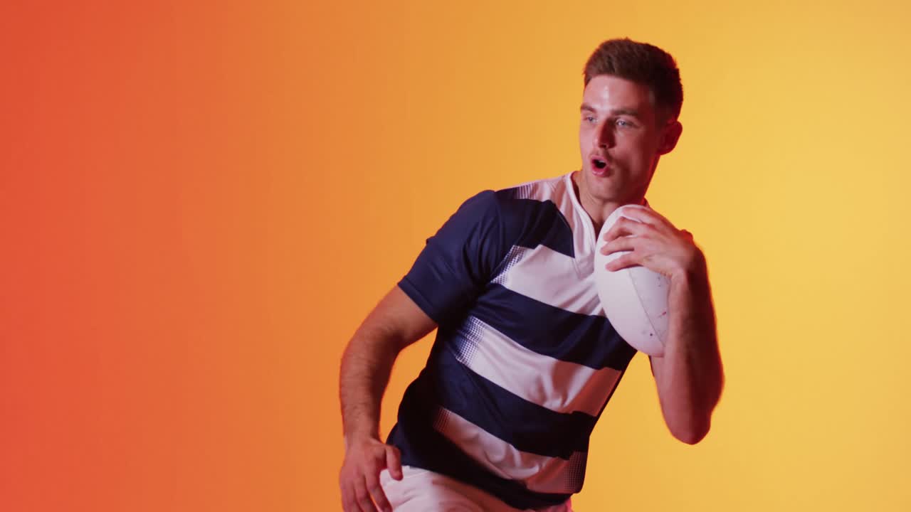 jugador de rugby masculino caucásico con pelota de rugby sobre iluminación naranja