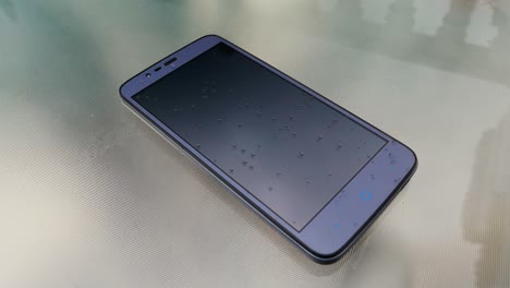 modern smartphone resting on a glass table while raindrops fall on the screen