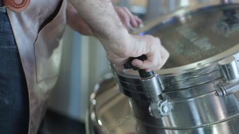 young male brewer wearing a leather apron supervise the process of beer fermentation at a modern brewery factory