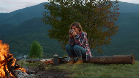 lonely traveler rest forest in mountains. relaxed woman drink tea by campfire.