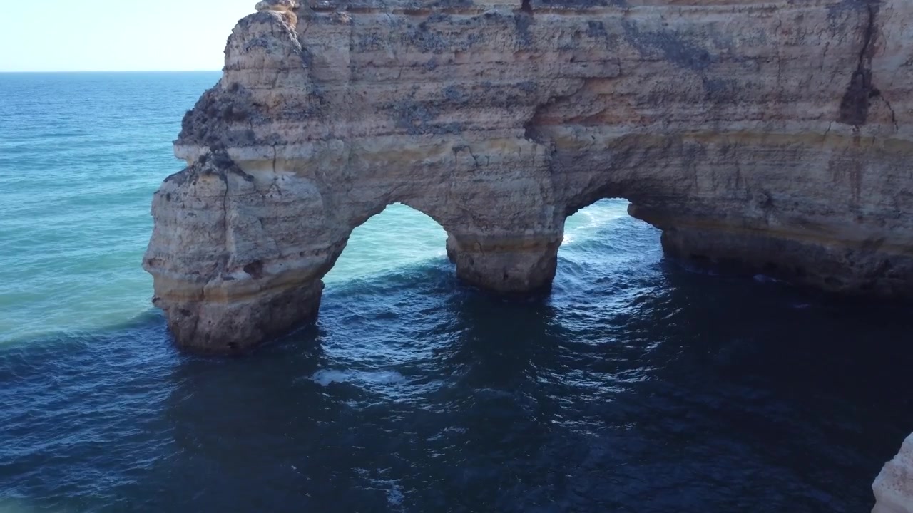 Stunning natural rock arches and caves along the beautiful coastline of Algarve, Portugal. Waves crash against the ancient cliffs on a bright sunny day.
