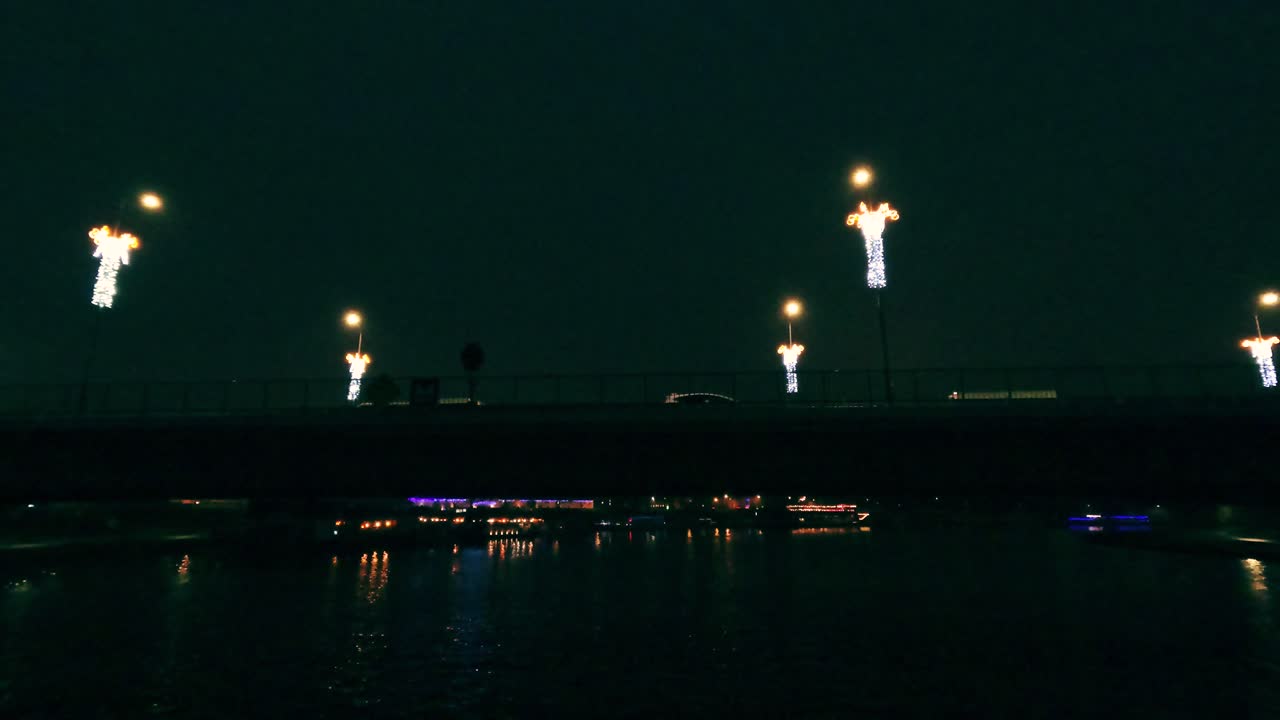 Le luci brillanti si alzano dal ponte sul fiume di notte. L'evento attira folle di persone che si godono la vista degli spettacoli colorati e dei riflessi sull'acqua.