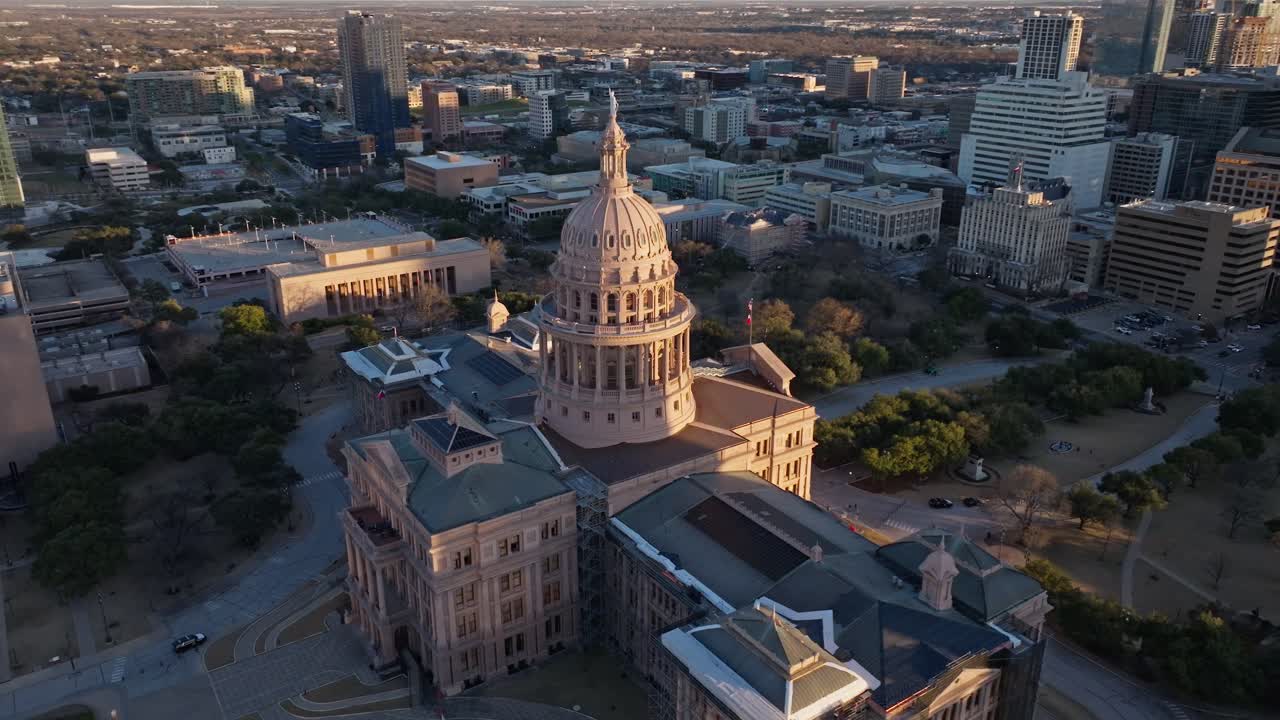 A drone shot slowly circling the Texas State Capitol building in Austin Texas at sunset facing away from the sun with the sun illuminating the Goddess of Liberty statue on top of the dome