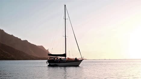 sail yacht at anchor off an island at sunset