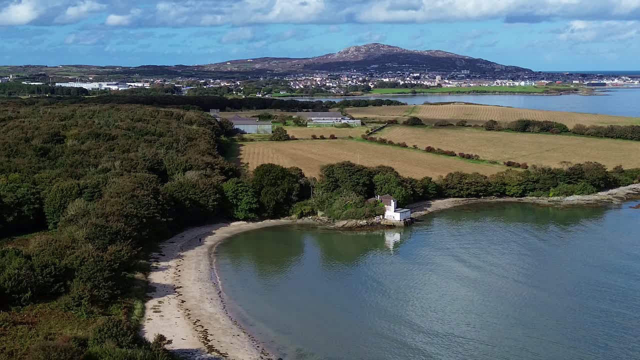 Aerial view establishing Welsh crescent bay under idyllic Holyhead mountain and distant farmland