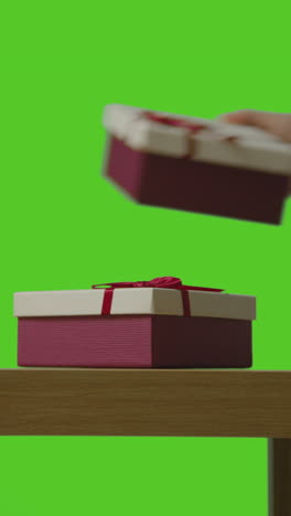 vertical video of man putting presents in gift wrapped boxes onto table shot against green screen