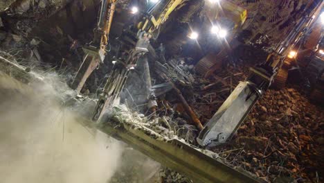 multiple crews working to demolish an old building at night using excavators with hydraulic pincers