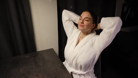 Stunning-young-woman-sitting-down-in-the-apartment-wearing-a-robe-puts-on-a-hair-tie-scrunchie