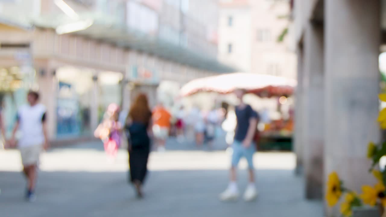 People walk past sunflowers and outdoor stalls in bright, sunny Nuremberg city center