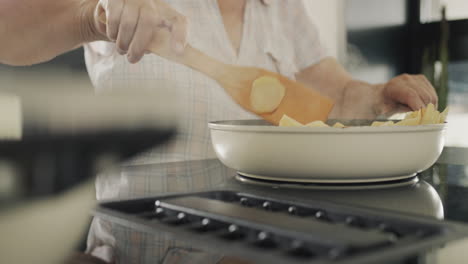 senior woman fries potatoes on an induction electric stove with a built-in extractor fan