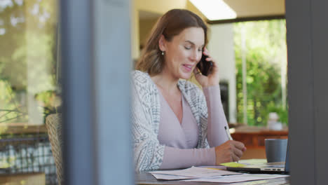 Mujer-Embarazada-Caucásica-Sentada-En-El-Escritorio,-Trabajando-Remotamente-Usando-Un-Teléfono-Inteligente-Y-Una-Computadora-Portátil