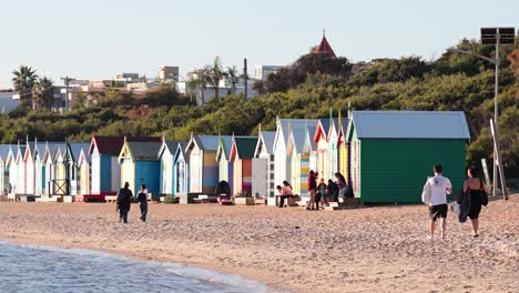 people walking along brighton beach with beach huts