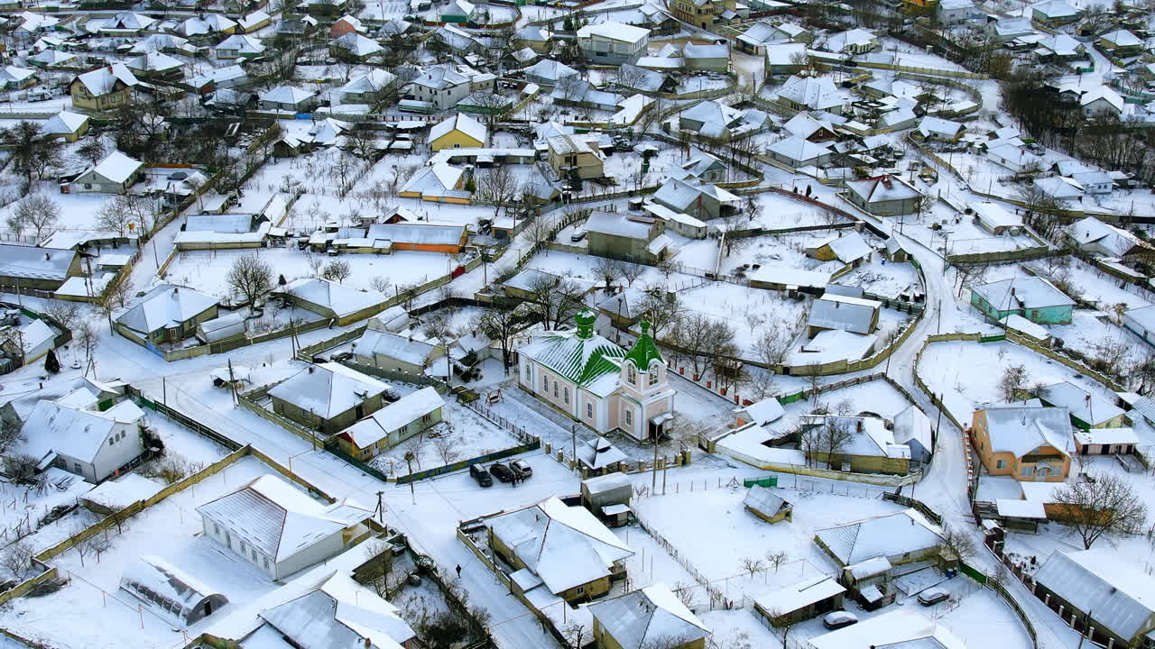 Kışın Moldova'daki bir köyün havadan drone görüntüsü. Karla kaplı yerleşim binaları, kilise ve yollar, çıplak ağaçlar