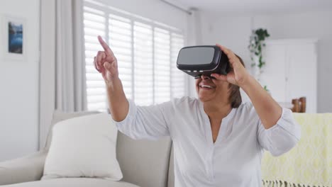 Happy-african-american-senior-woman-sitting-on-couch-enjoying-using-vr-headset