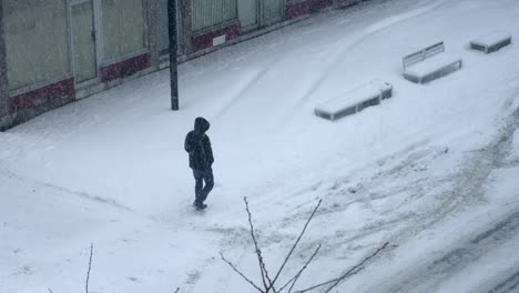 Mann-Im-Kapuzenpulli-Geht-Tagsüber-Bei-Kaltem,-Stürmischem-Schneefall-4k-Am-Gebäude-Vorbei