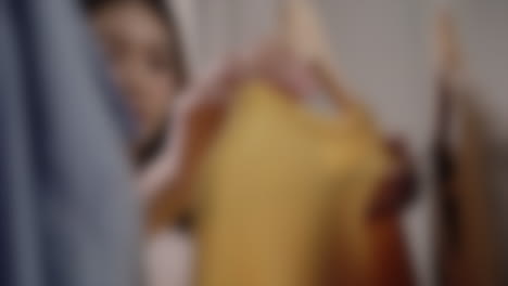 Blurred-close-up-shot-of-woman-shopping-for-clothing,-taking-pieces-of-clothes-off-from-the-clothes-hangers