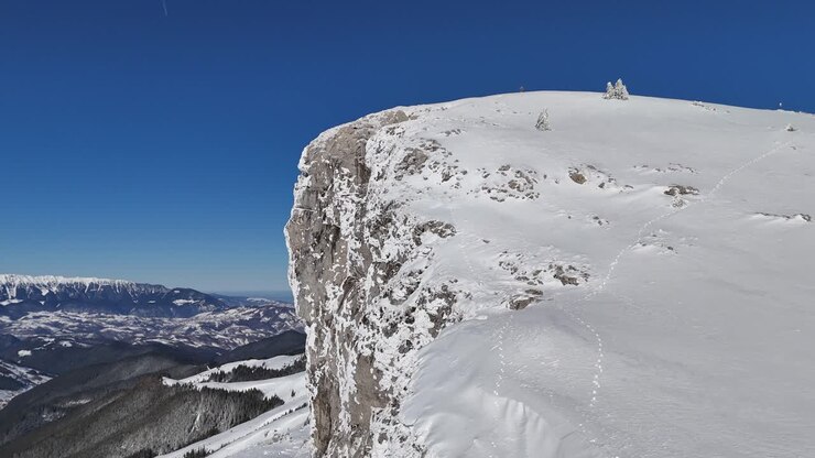 Snow-capped Bucegi Mountains under a clear blue sky, sunlight casting shadows on the peaks