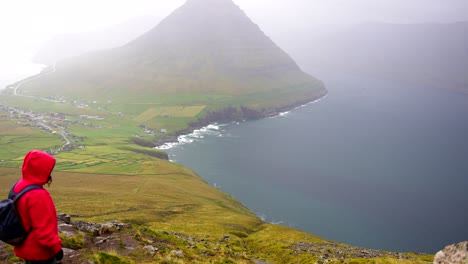 Panning-left-shot-of-a-woman-looking-at-the-foggy-Vidareidi-village-and-Malinsfjall