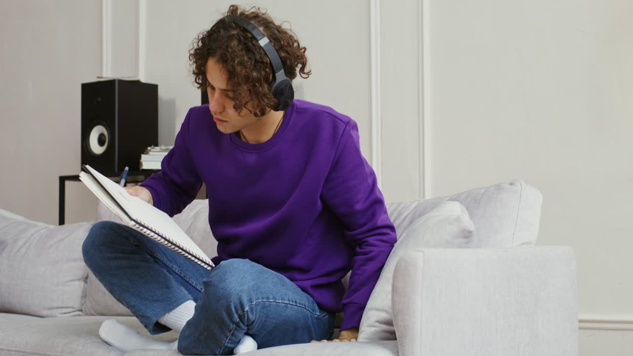 Young Man Sketching on a Couch While Listening to Music