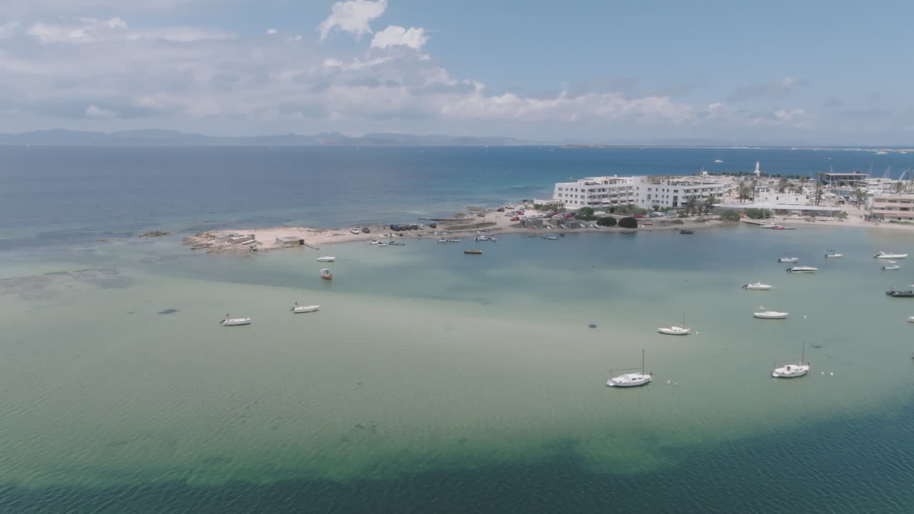 Drone flight entering from the sea through the Sa Boca inlet, revealing the full panorama of La Savina port and village on a bright Mediterranean day