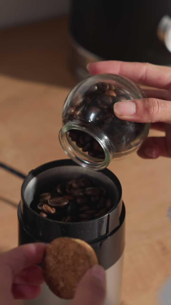 여성은 테이블에서 는 기계에 커피 콩을 추가합니다. 여자는 주방 장치에 구운 곡물을 넣고 음료 준비를 시작합니다. 향기적인 의식이 시작됩니다.