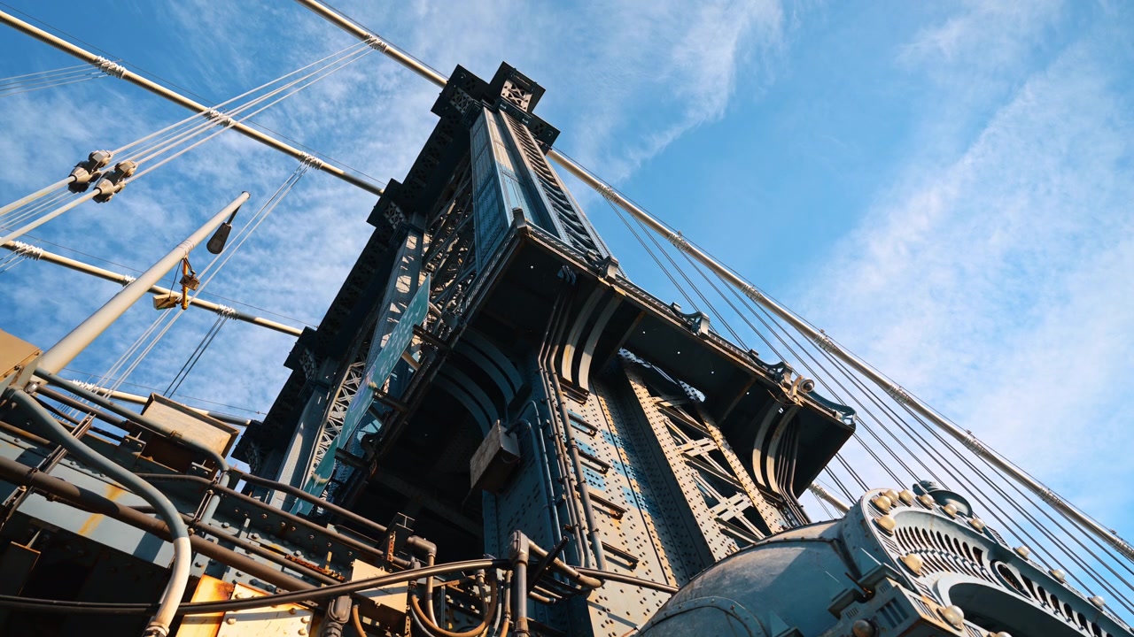 Steel tower and cables of Manhattan Bridge from below. A wide low angle composition emphasizes rivets, trusses and diagonal suspension lines.
