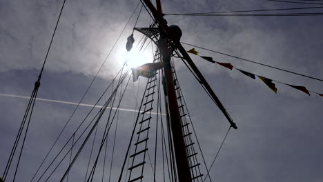 Blick-Nach-Oben-Zu-Einem-Segelbootmast-Mit-Der-Sonne-Im-Hintergrund-Und-Wehenden-Flaggen-In-Zeitlupe